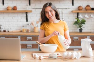 Woman baking at home mixing cake batter in kitchen with baking ingredients around