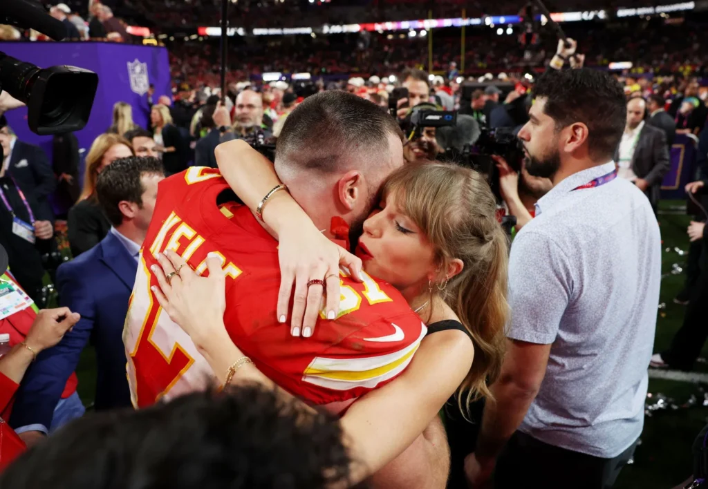 Taylor Swift embraces Travis Kelce on the field after a championship victory, showcasing a historic milestone in the Travis and Taylor relationship timeline.